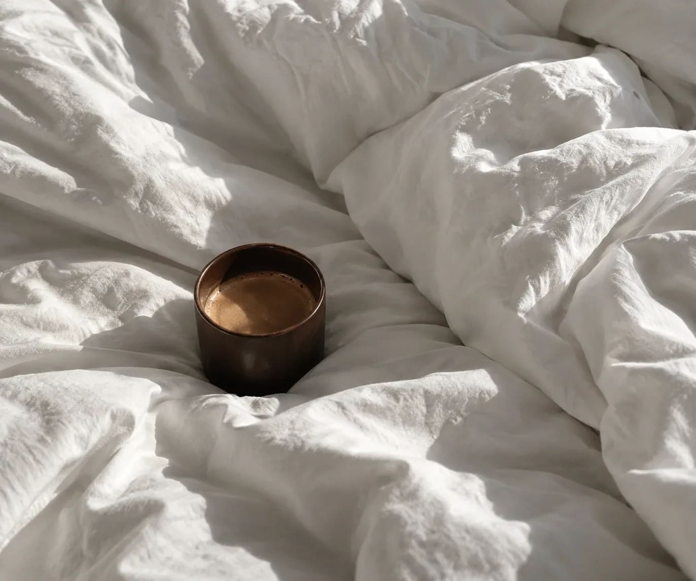 Dampfende Tasse in zerknitterter weißer Bettwäsche im Morgenlicht
